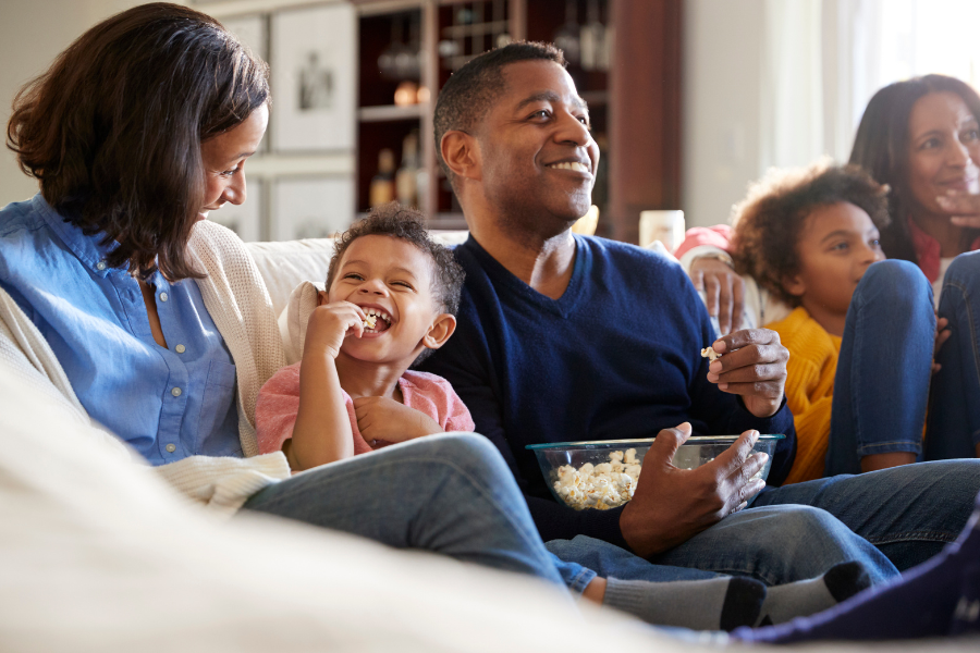 Family sitting on a couch eating popcorn and smiiling